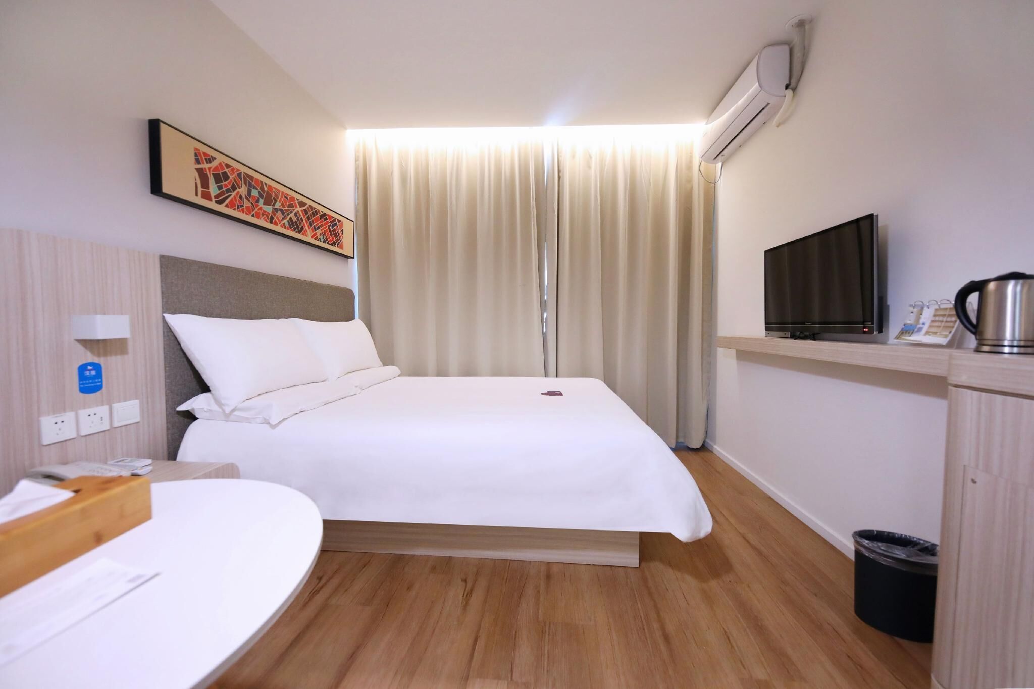 Una habitación de hotel con cama, escritorio con teléfono, televisor y aire acondicionado.