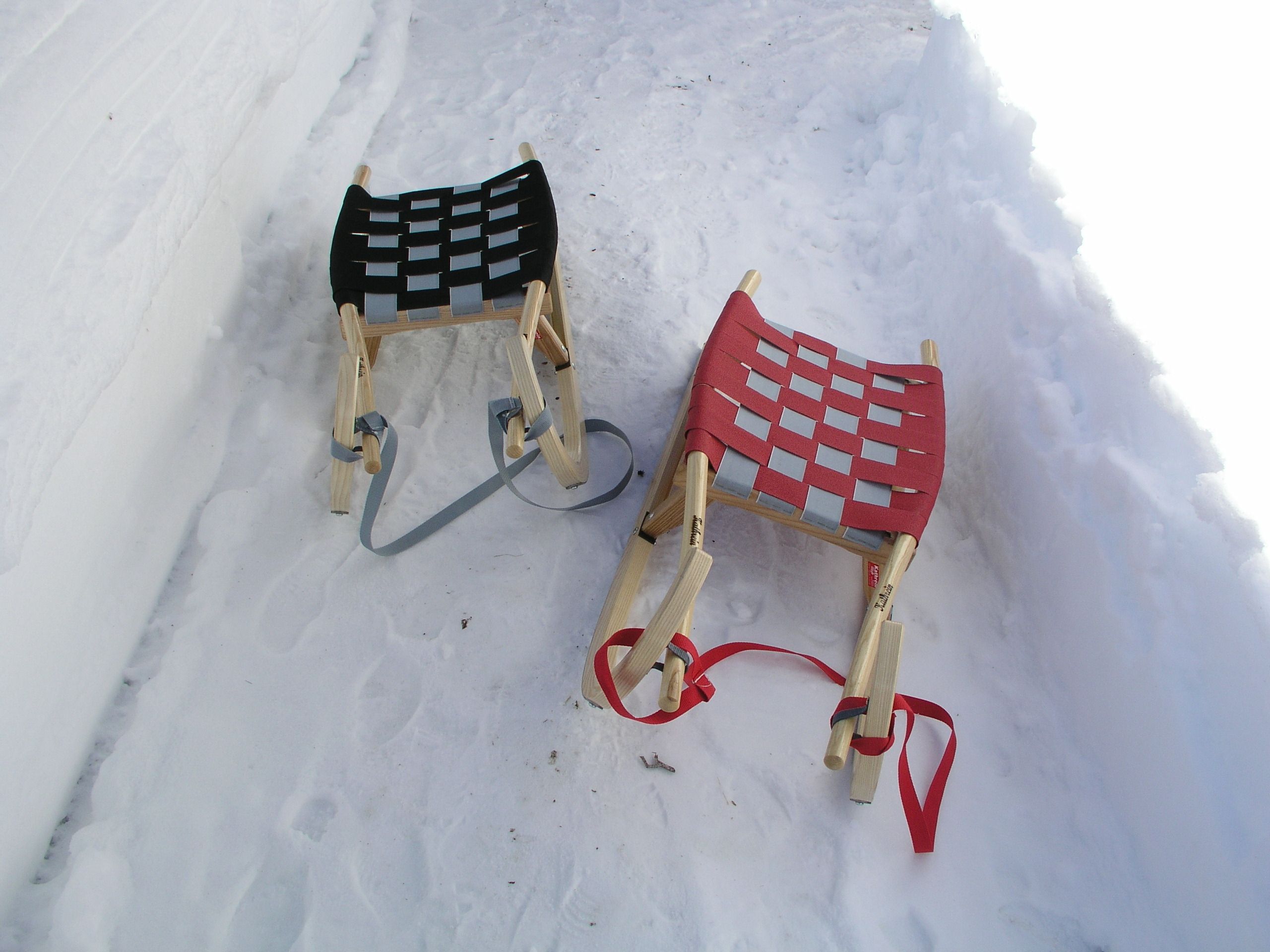 Two wooden sleds with woven seats and bindings, lying on snow.