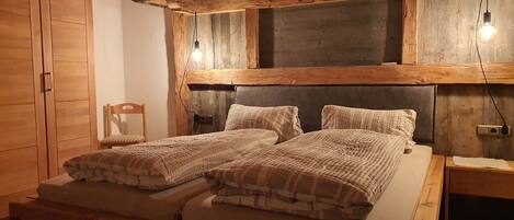 Una cama de madera con cabecera, dos mesitas de noche, una silla y un armario en una habitación rústica.