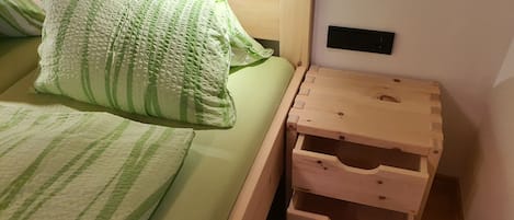 A bed with green striped bedding, a wooden nightstand with drawers, and a wall-mounted electrical outlet.