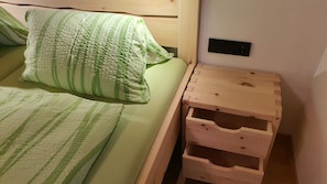 Un lit avec une literie à rayures vertes, une table de chevet en bois avec des tiroirs et une prise électrique fixée au mur.