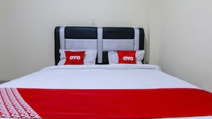 A hotel room with a bed, two pillows with the brand name "OYO", a red and white bedspread, and a white wall with a power outlet.