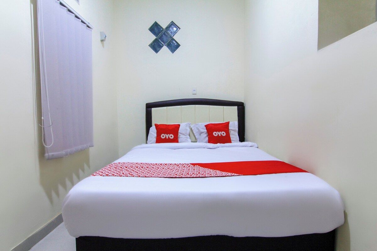 Habitació d'hotel estreta amb un llit, una làmpada penjada a la paret i una finestra amb cortina.