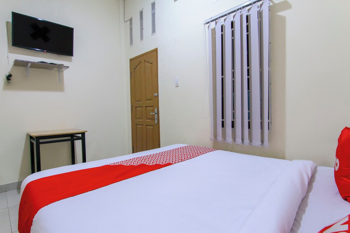 A room with a bed, a television mounted on the wall, a door, and a window with blinds.