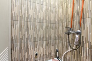Zona de ducha con pared de azulejos, cabezal de ducha de mano y manguera flexible.