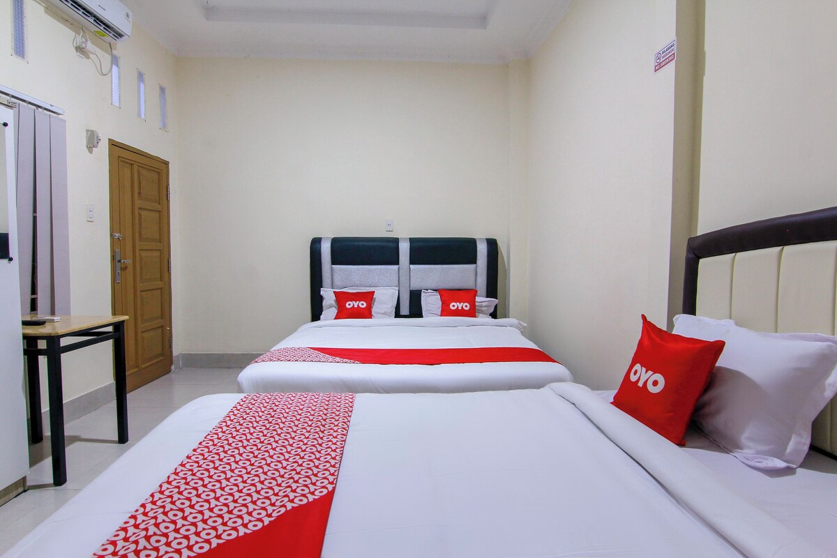 A hotel room with two beds, a wooden door, a small table, and a wall-mounted air conditioner.
