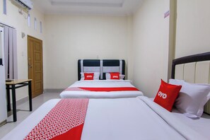 A hotel room with two beds, a wooden door, a small table, and a wall-mounted air conditioner. - Ratu Residence (Medan)