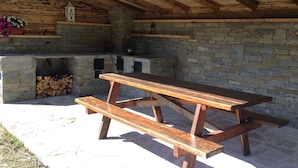 A wooden picnic table with benches, a stone fireplace, and a lantern on a stone wall.
