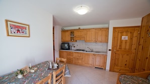 A compact kitchen with wooden cabinets, a dining table with chairs, and a bed in the adjacent room.