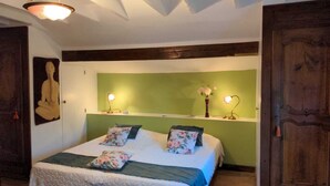 Ein Schlafzimmer mit einem Bett, grünen Wänden, Holzbalken, einem Gemälde und zwei Nachttischlampen.