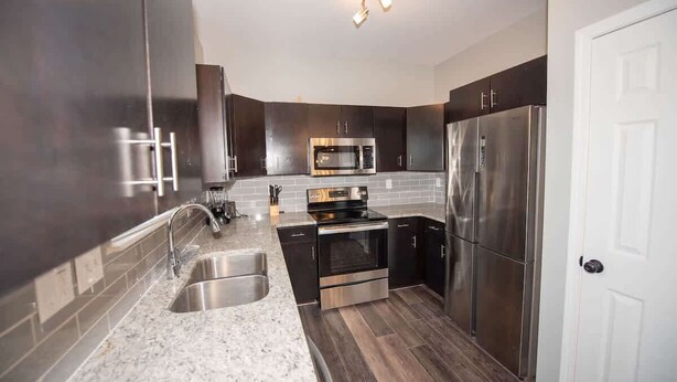A modern kitchen with stainless steel appliances, a granite countertop, and dark cabinetry.