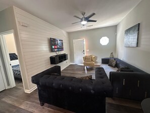 A living room with a flat-screen TV, a ceiling fan, and a sofa.