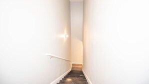 A narrow stairway with white walls and a handrail, leading to a landing.