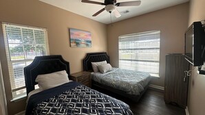 A bedroom with two beds, a ceiling fan, a painting, and a TV.
