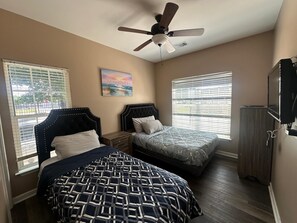 Una camera da letto con due letti, una ventola a soffitto, un quadro e una TV.