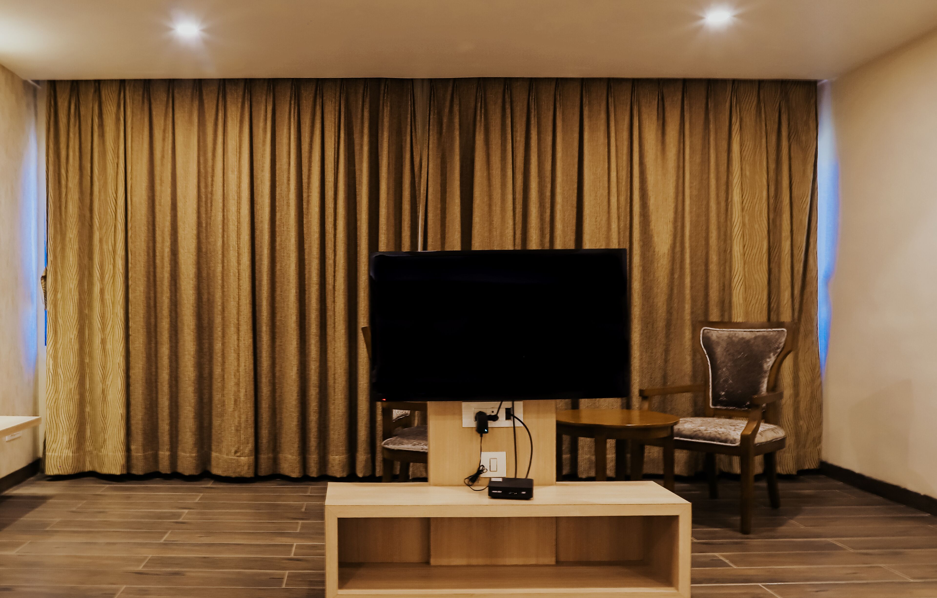 Ein Zimmer mit einem Flachbildfernseher an einem Holzständer, einem Sessel und einem großen Vorhang.