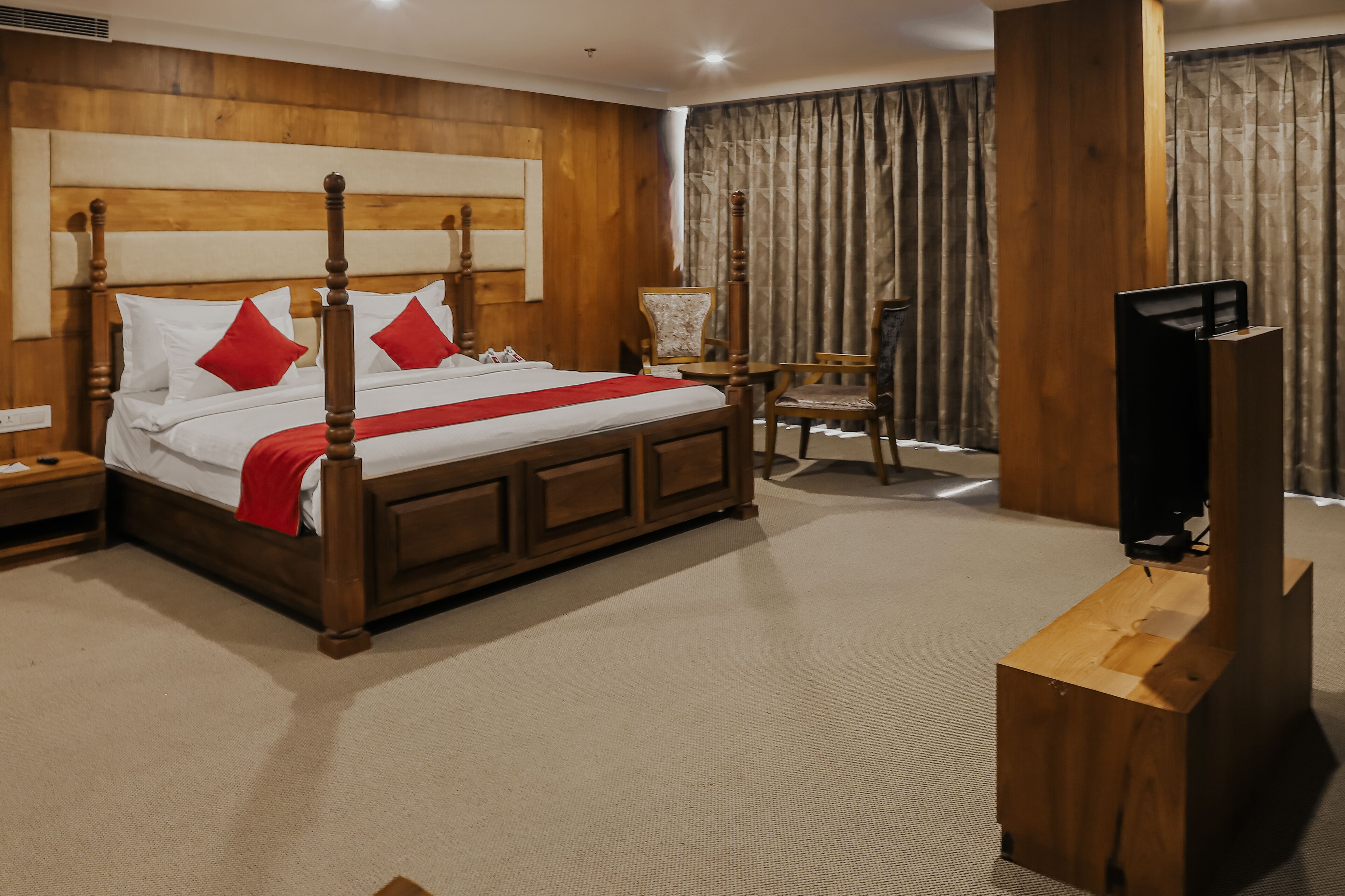 Une chambre d’hôtel avec un lit à baldaquin, une tête de lit en bois, une télévision, une chaise et une table de chevet.