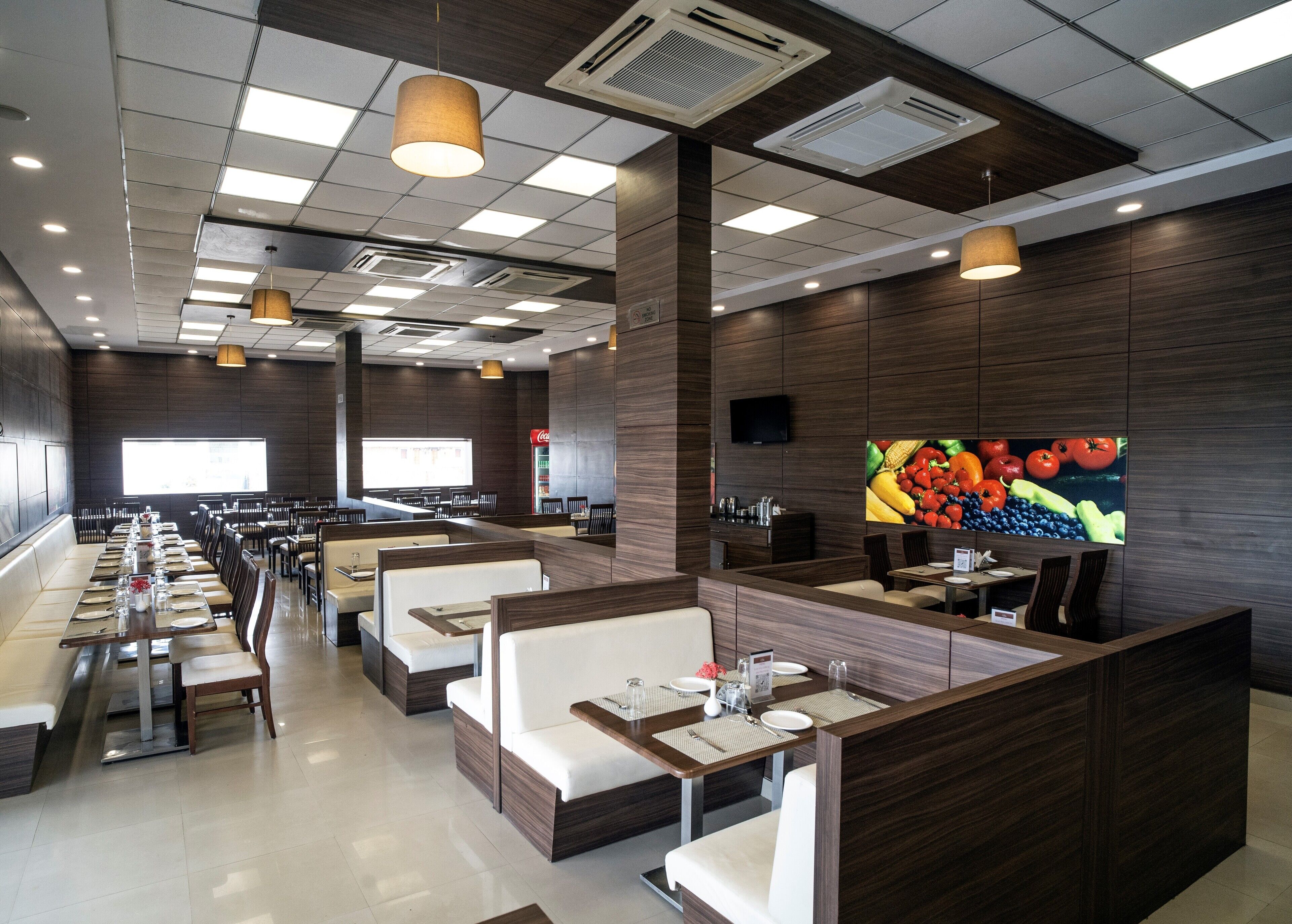Een modern restaurant met zitbankjes, een groot televisiescherm en een muurschildering met fruitmotieven.