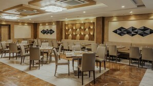A modern dining area with multiple tables and chairs, recessed lighting, and decorative wall panels. - Regenta Central Somnath (Veraval)