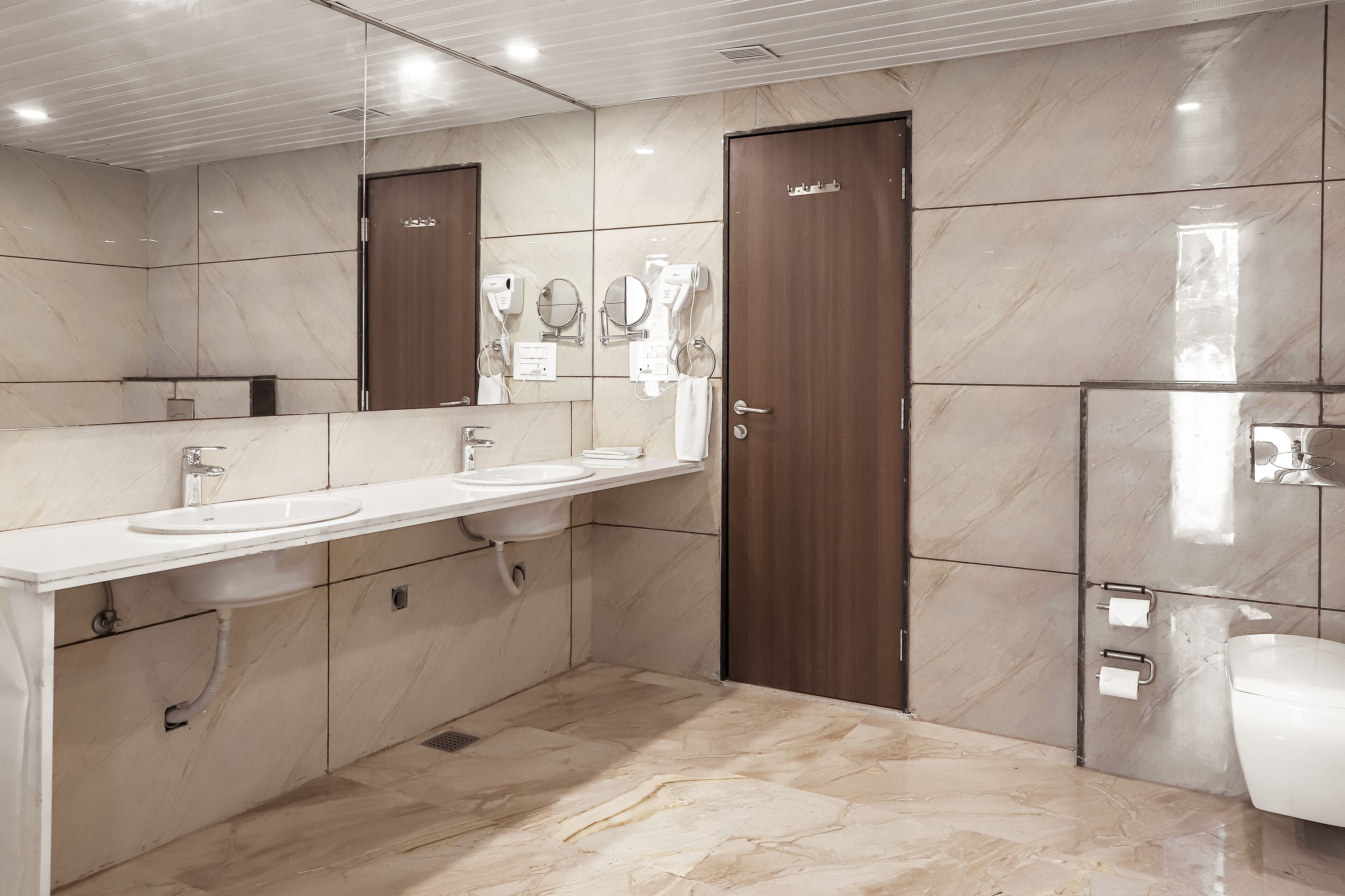 A modern bathroom with a white sink, a large mirror, and a wooden door.