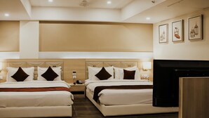 A hotel room with two beds, a flat-screen TV, a bedside table, and a wall-mounted lamp. - Regenta Central Somnath (Veraval)