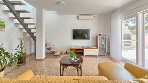 Ein Wohnzimmer mit Treppe, Flachbildfernseher, Essbereich und einer Schiebeglastür zum Außenbereich.