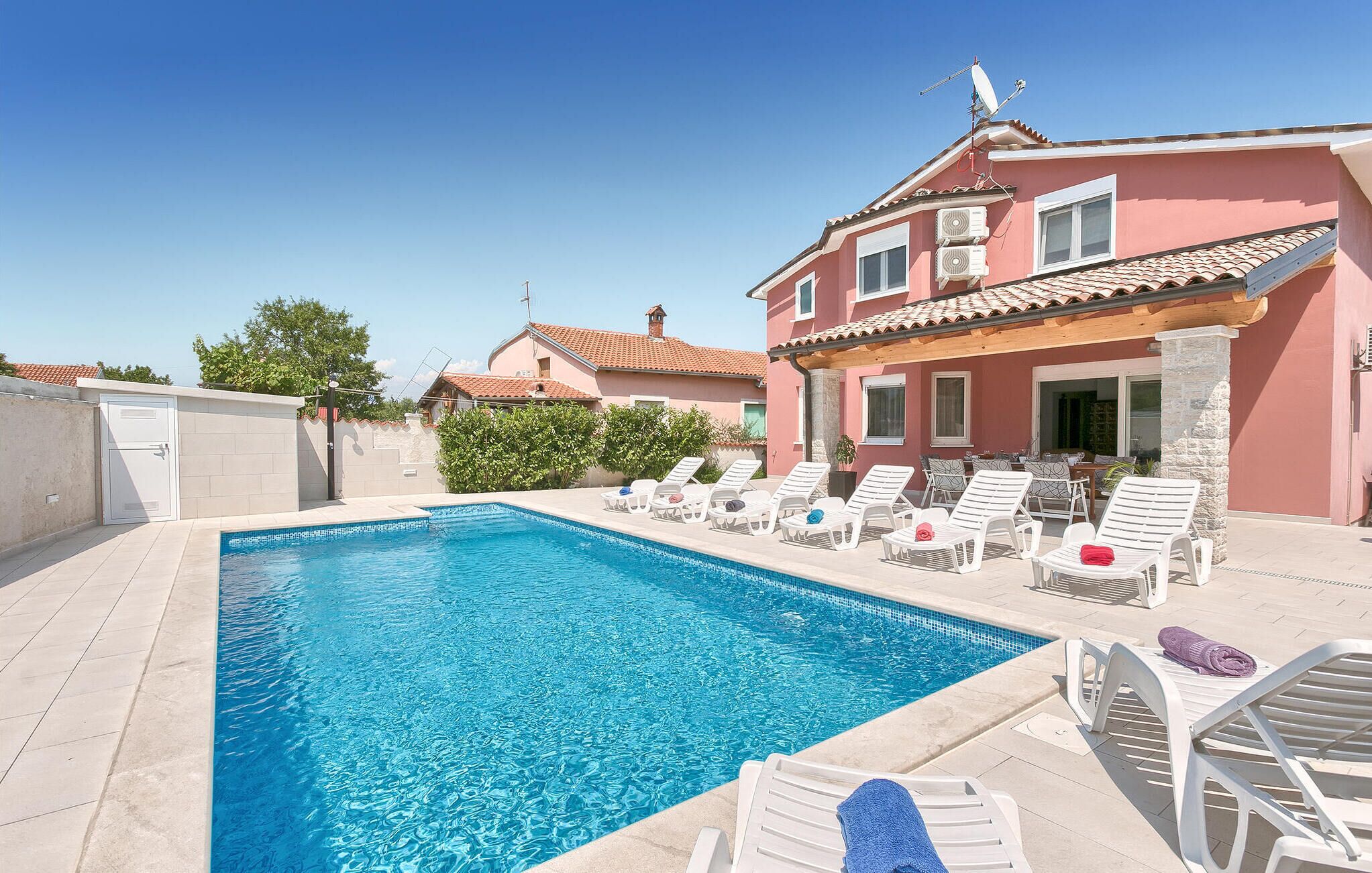 A swimming pool with lounge chairs, a building with a red facade, and a clear blue sky.