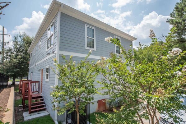 A two-story house with a front porch, a garage, and a small yard with trees.