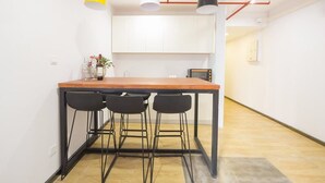 A modern kitchen with a wooden table and black chairs, white cabinets, and pendant lighting.