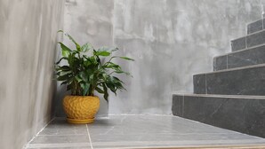 A corner with a potted plant on a tiled ledge, a marble wall, and a staircase with dark tiles.