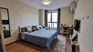 A modern hotel room with a large bed, a desk, a chair, a TV, and a window with a view.