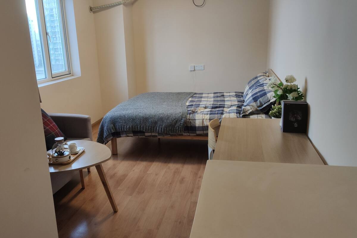 A small, cozy room with a bed, a table with a tray of tea, and a window.