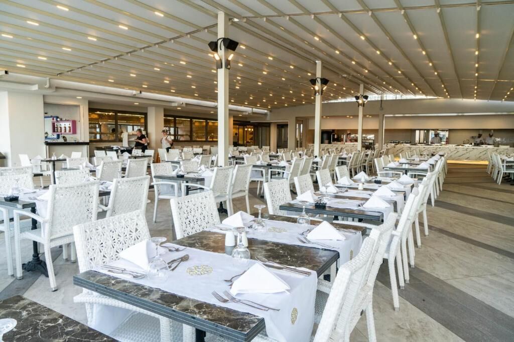 A spacious dining area with white chairs and tables, a high ceiling with lights, and a modern interior design.