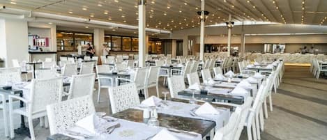 A spacious dining area with white chairs and tables, a high ceiling with lights, and a modern interior design.