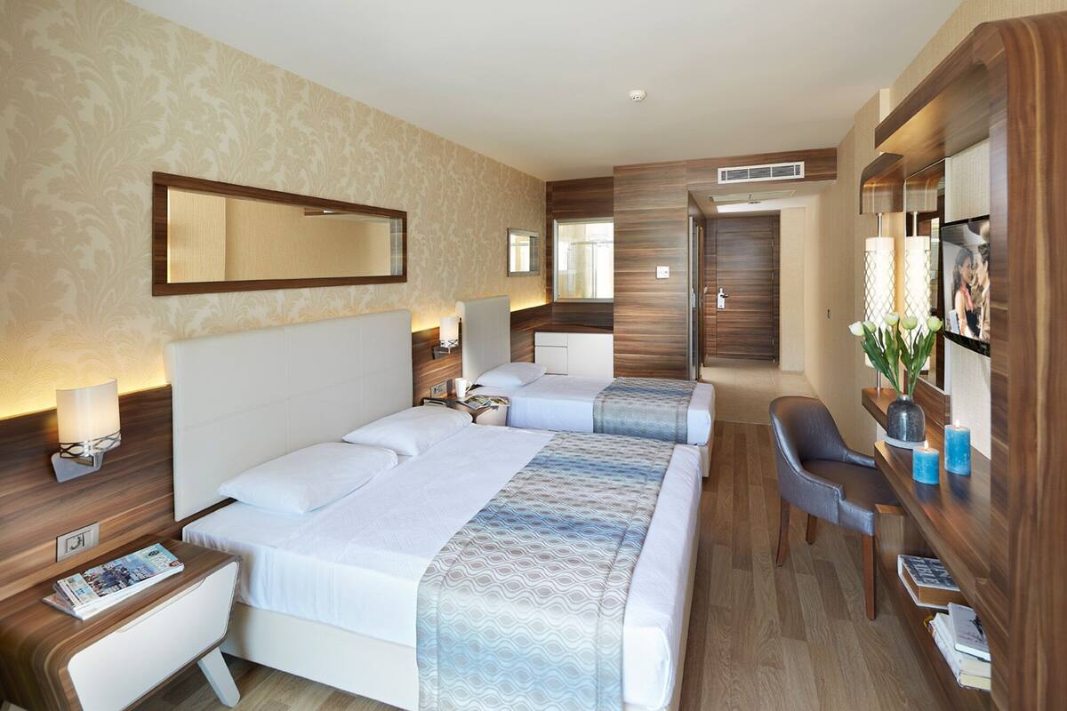 Quarto de hotel com uma cama grande, mesas de cabeceira, escrivaninha e uma cadeira.