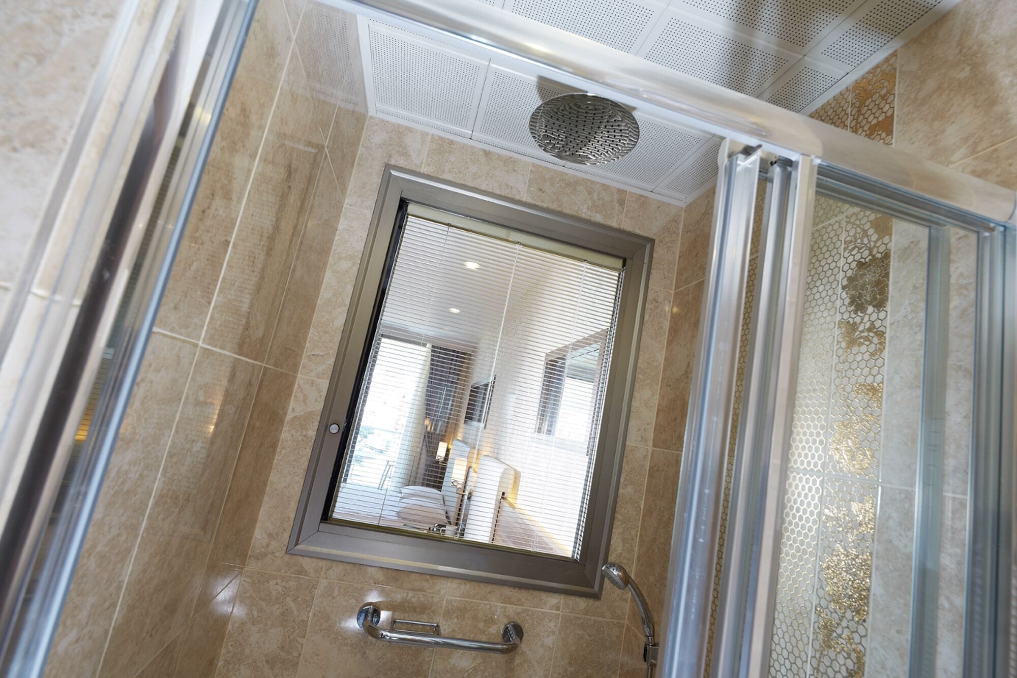 A shower with a glass door, a handrail, and a ceiling vent.