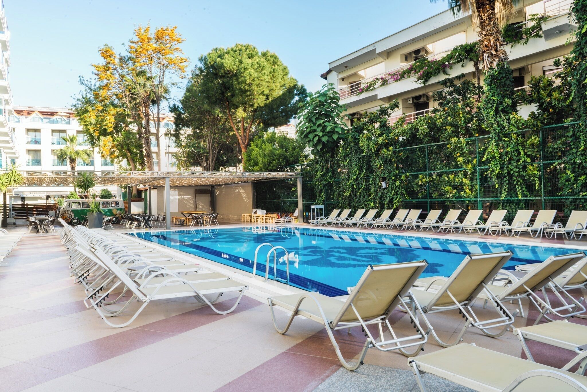 A swimming pool with lounge chairs and a sun deck, surrounded by greenery and buildings.