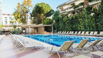 A swimming pool with lounge chairs and a sun deck, surrounded by greenery and buildings.