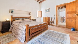Ein Schlafzimmer mit einem hölzernen Bett, einem Nachttisch, einer Lampe, einem Holzschrank und einer Tür zu einem anderen Raum.