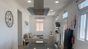 A modern kitchen with a central island, a dining area with a sofa, and a living space with a TV. - Casa da Paz - Fantastic view of Funchal Bay (São Gonçalo)