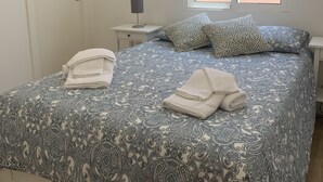 A neatly made bed with patterned bedding, a bedside lamp, and a window with blinds. - Casa da Paz - Fantastic view of Funchal Bay (São Gonçalo)