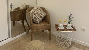 A room with a wicker chair, a round ottoman, a small table with cups and glasses, and a mirror reflecting the room. - Casa da Paz - Fantastic view of Funchal Bay (São Gonçalo)