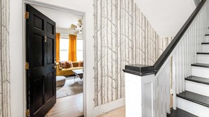 Un escalier avec une rampe noire et des marches blanches, menant à une pièce dont le papier peint est orné de motifs et dont la porte porte le numéro « 2 ».