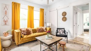 Un salon lumineux avec un canapé jaune, une table basse et un fauteuil noir.