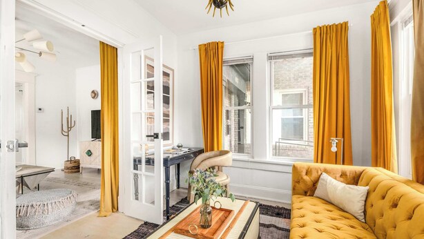 Une pièce avec un canapé jaune, une table basse en bois sur laquelle se trouve un vase, et un bureau avec une chaise.