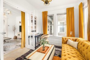 A room with a yellow sofa, a wooden coffee table with a vase, and a desk with a chair. - Morefunk (Atlanta)