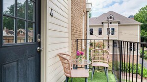 Une maison avec une porte noire, un mur en briques et un petit balcon agrémenté de deux fauteuils en osier et d’une table.
