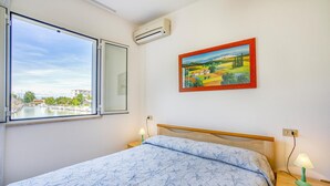 A bedroom with a bed, a window with a view of a marina, an air conditioner, a painting, and a bedside lamp. - 1 bedroom stunning apartment in Caorle (Caorle)