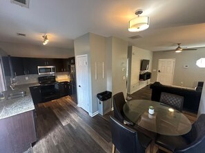 A modern kitchen with dark cabinetry, a microwave, and a refrigerator. There is a dining area with a glass table and chairs.