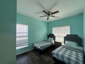 A room with two beds, a ceiling fan, and windows with blinds.